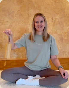 Lisa sitzt auf ihrer Yogamatte und hält ein Klanginstrument